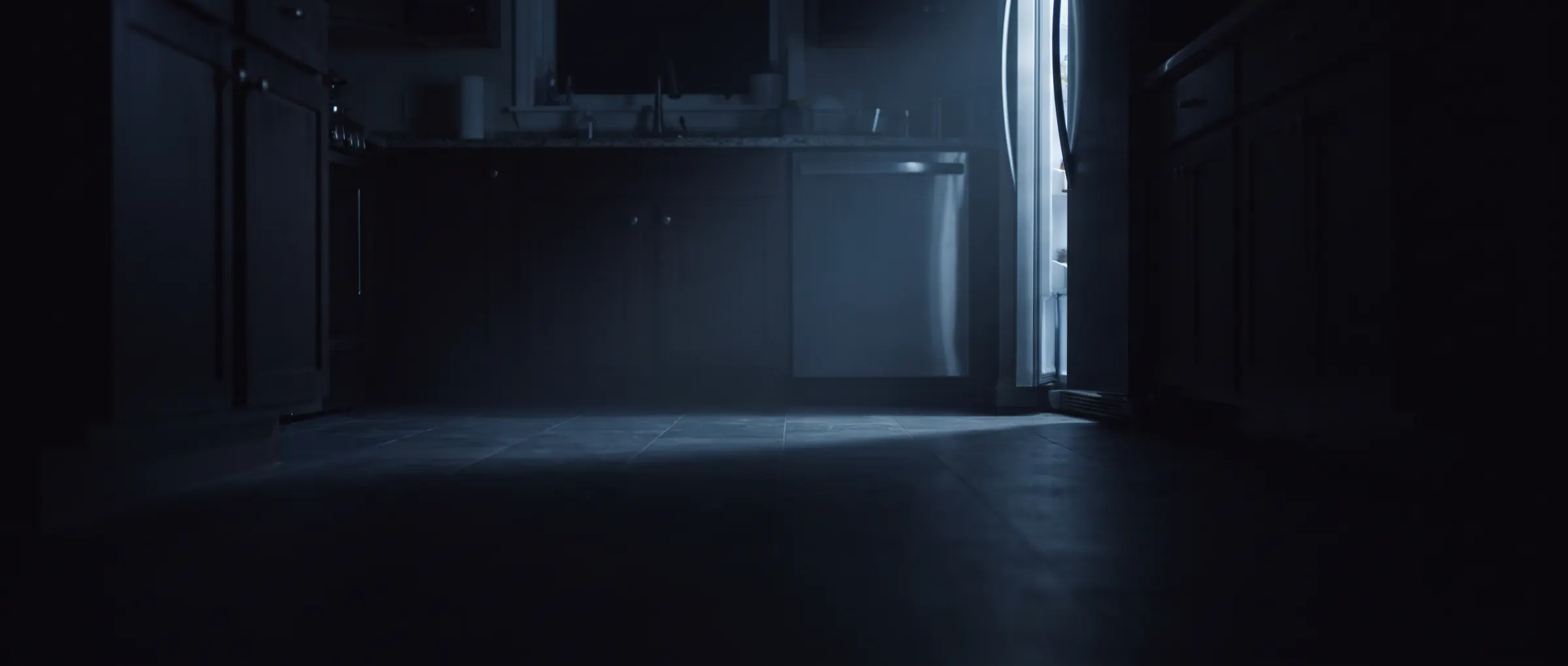 A dark kitchen at night, lit only by the open door of a refrigerator