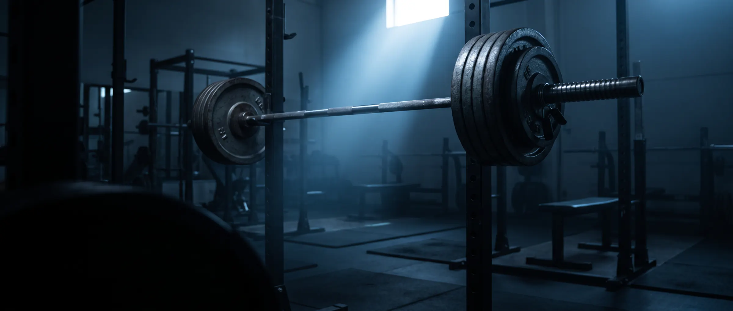 A loaded barbell resting in a squat rack in a dark, empty gym