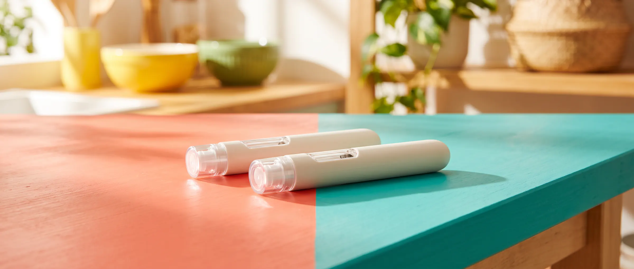 Two plain injection pens side by side on a two-colour table