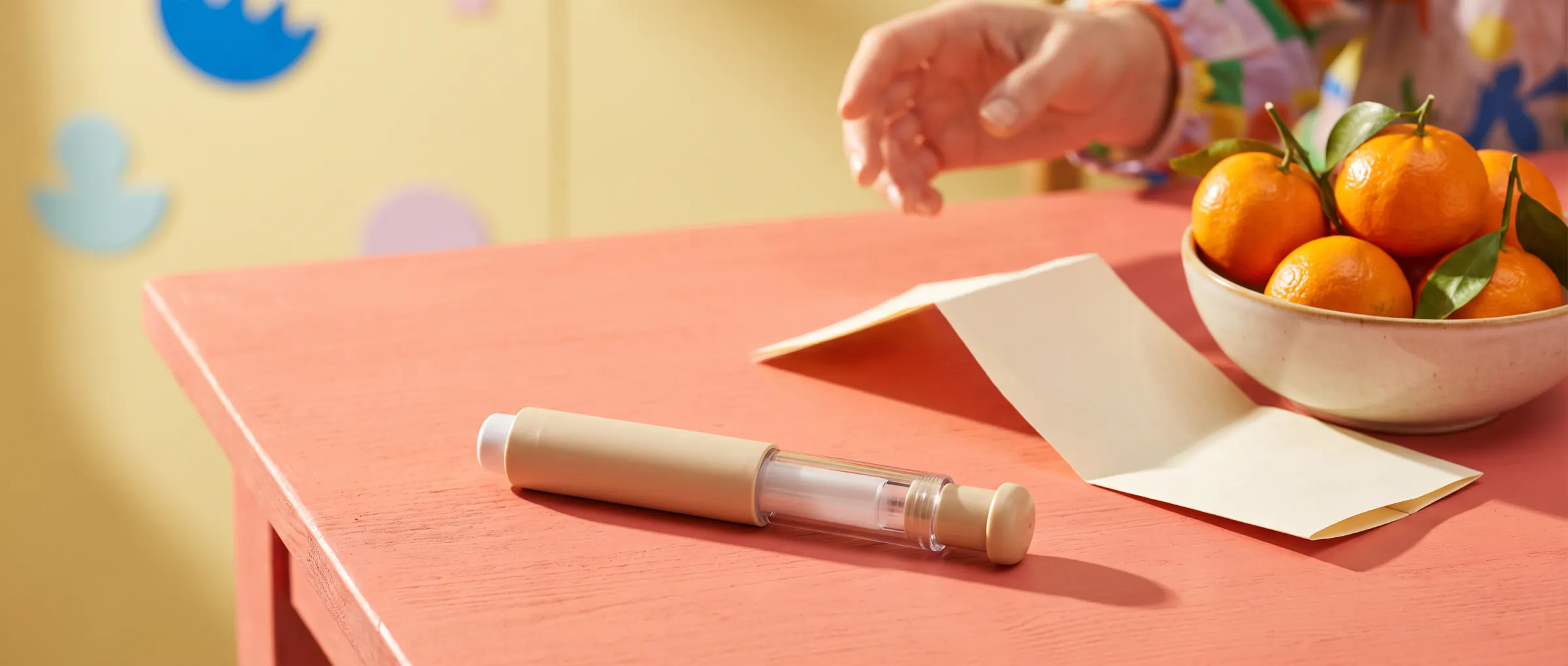 An injection pen beside a folded paper leaflet on a sunny coral table